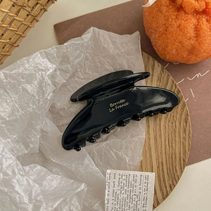 Macro detail of glossy black hair claw clip with gold lettering on a wooden tray