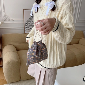 Close-up of a floral corduroy drawstring bag held by a person in a cozy home setting