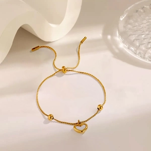Close-up of golden heart charm bracelet with adjustable slide clasp on elegant background