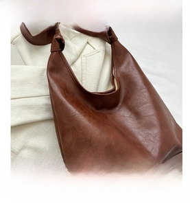 Detail view of large brown tote bag with decorative knot shoulder strap and faux leather texture