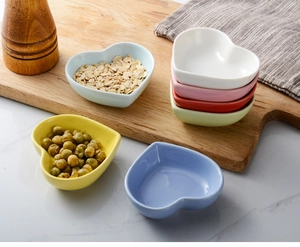 Colorful heart-shaped ceramic dipping bowls arranged on a wooden board and marble surface