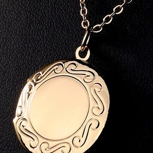 Vintage gold oval locket necklace with embossed scroll pattern on black leather background