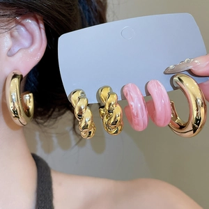 Macro detail of gold twisted hoop earrings and pink marble resin ring set