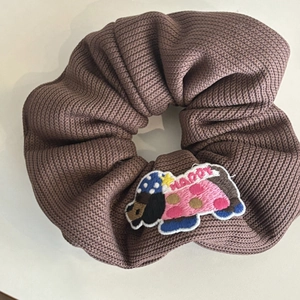 Close-up of knitted brown scrunchie with cute dog embroidery and Happy text detail