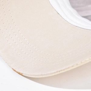 Detailed close-up showing reinforced curved stitching on a beige canvas baseball cap brim