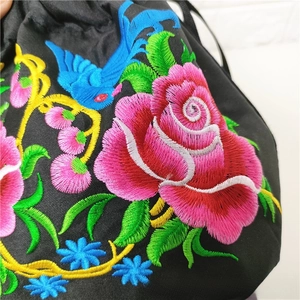 Detailed view of colorful bird and floral embroidery on black drawstring bucket bag