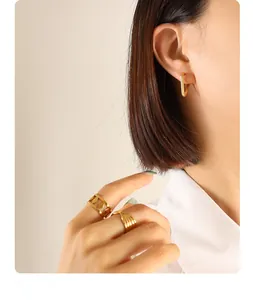 Detailed close-up of golden U-shaped earrings and minimalist rings on a model
