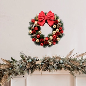 Christmas wreath with red bow, pine cones, and gold balls on a minimalist white wall