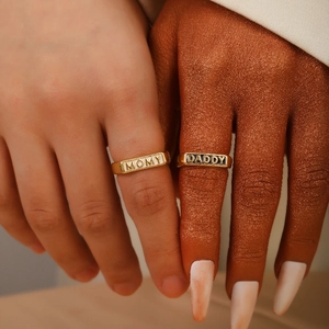 Close-up of gold MOMY and DADDY rings with engraved plaques for meaningful family gifts