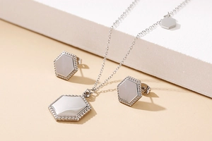 Detail of silver hexagonal jewelry set with necklace and stud earrings on white surface