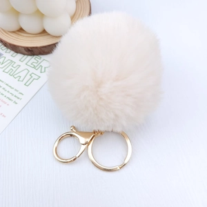 Close-up of fluffy beige faux fur pompom keychain with gold lobster clasp and metal ring