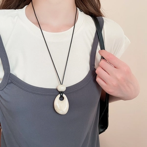 Detail of a minimalist ivory acrylic pendant on a black cord necklace worn by a model