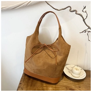 Detail of a brown faux suede tote bag with a knotted bow on a rustic wooden table