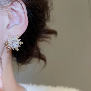 Close-up of elegant gold snowflake stud earrings with sparkling zircon crystals on model