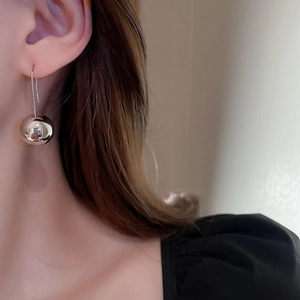 Close-up of a silver metal ball earring with long hook on a model for a minimalist look