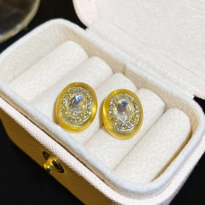 Macro shot of oval gold-plated stud earrings with crystal inlay on beige jewelry box