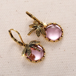 Detailaufnahme von Retro-Libellenohrringen mit rosa Mondsteinperlen auf Stoff
