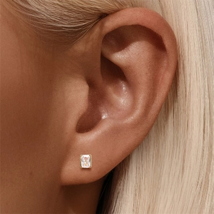 Close-up of a square cut clear gemstone earring with gold bezel setting on ear