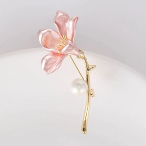 Macro detail of a pink metal flower brooch with golden stem and a white pearl accent