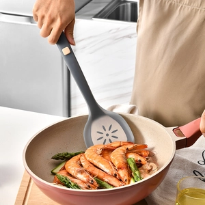Gray silicone spatula with flower-shaped holes used for frying prawns in a modern kitchen