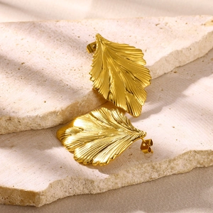 Macro shot of gold leaf earrings with textured veins on a natural stone surface
