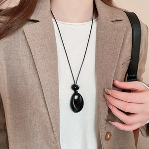 Close-up of a vintage black acrylic drop pendant necklace styled on a khaki suit jacket