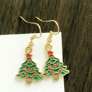 Detailed view of Christmas tree earrings with green enamel and gold hooks on wood background