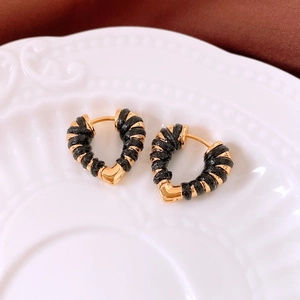Detail of 18k gold heart hoop earrings with black woven wrap on white ceramic plate