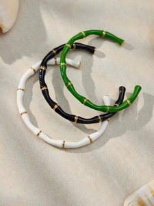 Dettaglio di tre bracciali stile bambù in smalto nero, bianco e verde a forma di C