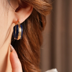 Dettaglio di orecchini geometrici in smalto blu e oro indossati da una modella