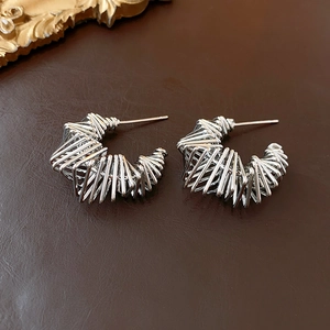 Macro view of silver-finish C-shaped twisted wire hoop earrings on leather background