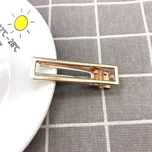Detail of a minimalist gold hollow rectangular metal hair clip on a white plate