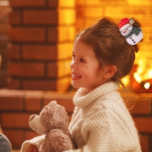 Cute snowman hair claw clip with red hat on girl's hair by a cozy fireplace