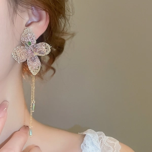 Dettaglio di orecchini a fiore in maglia rosa con nappe dorate e perline verdi