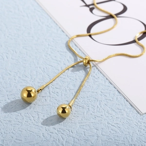Detail of adjustable gold snake chain necklace with sleek bead pendants on a blue surface