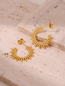Macro detail of 18K gold-plated C-shaped sunflower beaded earrings on travertine stone