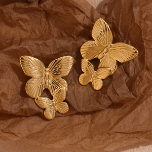 Detailed close-up of 18K gold plated butterfly earrings on textured vintage paper
