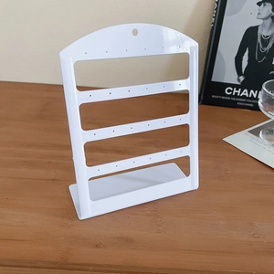 White acrylic earring holder stand with four tiers on wooden desk with elegant props
