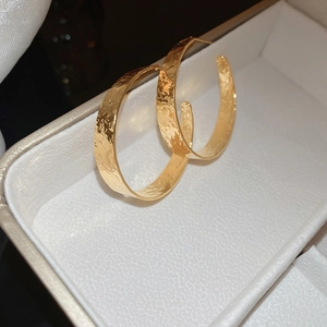 Macro detail of large golden hoop earrings featuring a unique hammered metal texture
