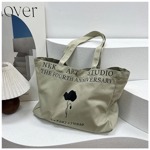 Close-up of a large beige canvas tote bag with black floral print on a textured background