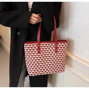 Red and white heart-pattern woven tote bag held by a model in a black winter coat