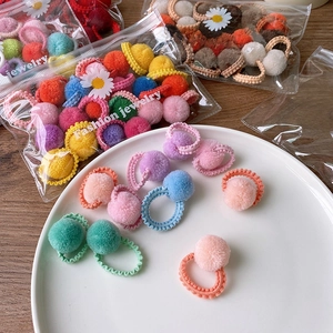 Detail of colorful plush pom pom hair ties in fashion jewelry packaging on white plate