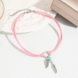 Detail of pink bohemian choker with silver feather pendants and blue bead on white surface
