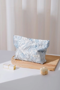 Detail of embossed floral jacquard makeup bag on a tray with cosmetics and candle