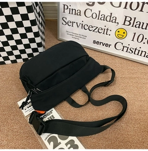 Detail of adjustable woven strap and plastic buckle on black nylon crossbody bag