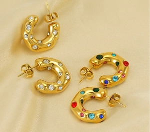 Detail of gold C-shaped earrings with clear and colorful rhinestones on beige fabric