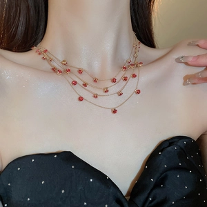 Detail einer mehrlagigen Goldkette mit roten Zirkonia-Anhängern am Hals getragen