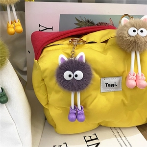 Close-up of fuzzy monster keychains with big eyes and colorful legs on a yellow bag