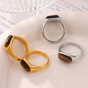 Geometrische Titanringe in Gold und Silber mit Tigerauge-Stein im Retro-Stil auf Keramik