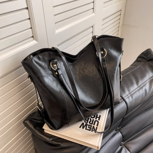 Large black faux leather tote bag with gold hardware placed on a leather sofa